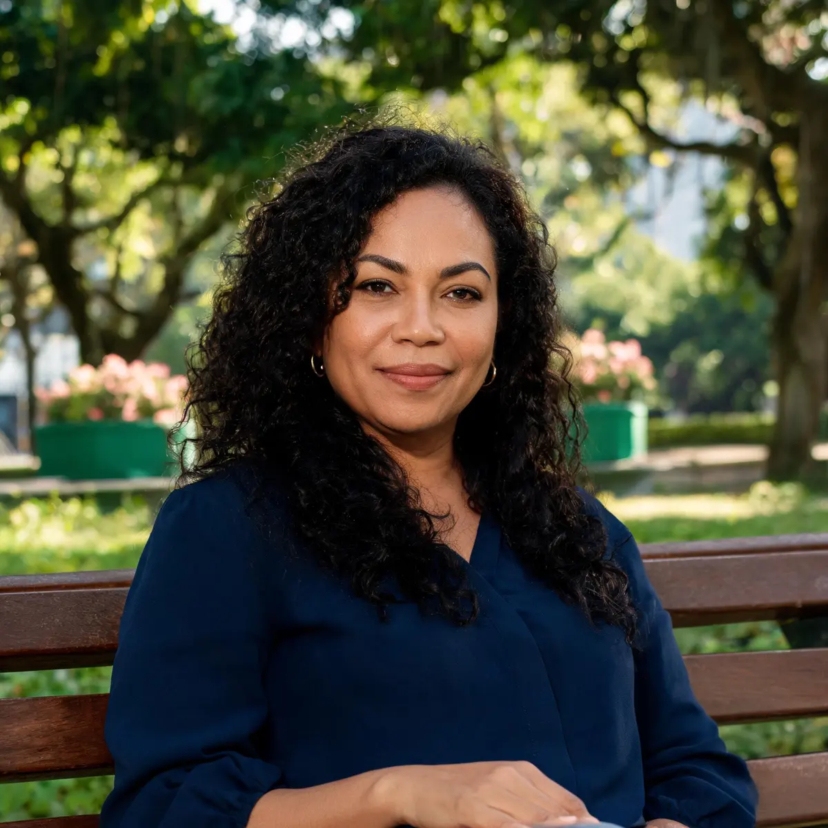 Mulher sorrindo, sentada num banco de praça arborizada (imagem ilustrativa)